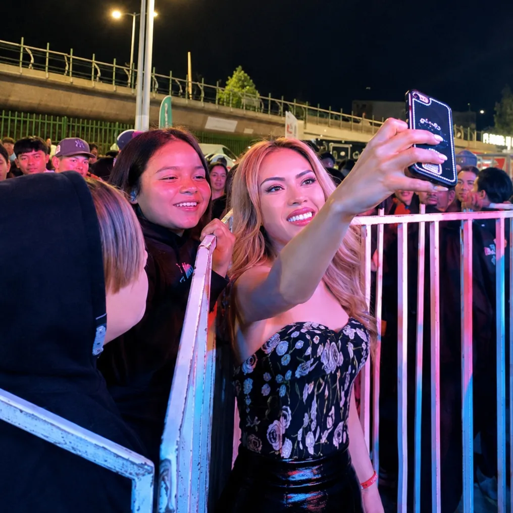 Bony sostiene un teléfono para tomarse una selfie junto a una joven y el público de un evento.